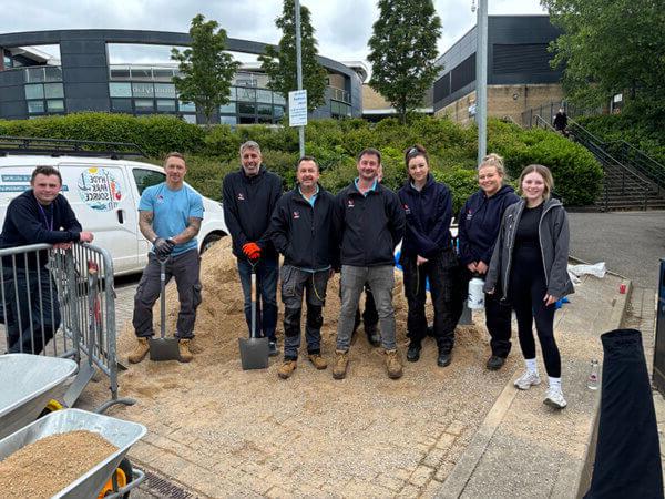 A group of smiling Mitie colleagues, standing in front of a pile of gravel and holding spades